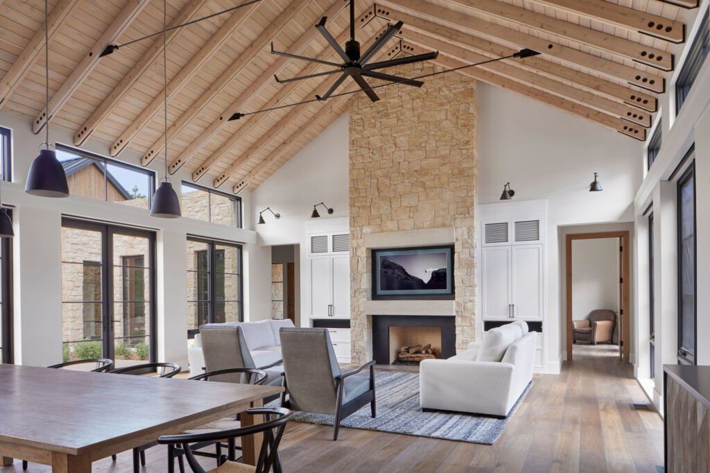 Modern farmhouse living room with vaulted ceilings, exposed wooden beams, and a cozy stone fireplace. Ideal inspiration for barndominium ceiling ideas.